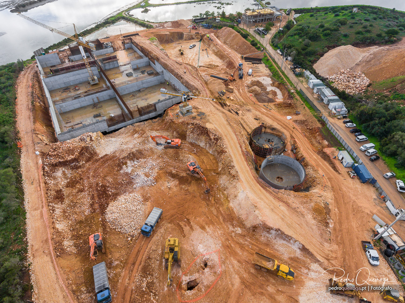 Vista aérea de grande estaleiro de obra com reservatórios circulares e estrutura principal junto à ria