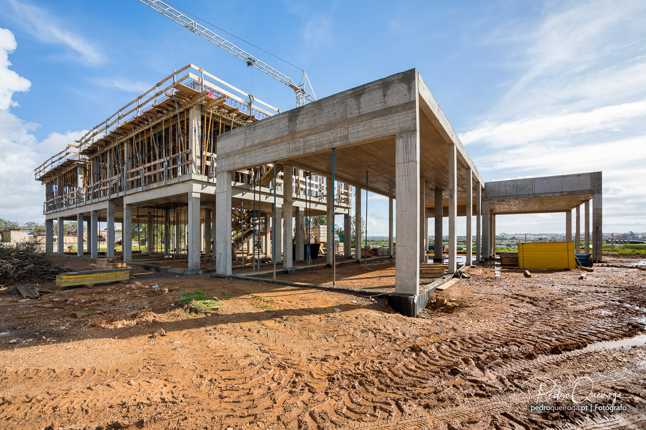Estrutura de betão armado com pilotis e lajes em construção sob céu azul no Algarve