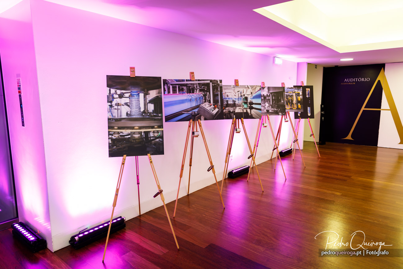 Exposição de fotografias industriais em cavaletes de madeira, com iluminação ambiente rosa num espaço interior moderno