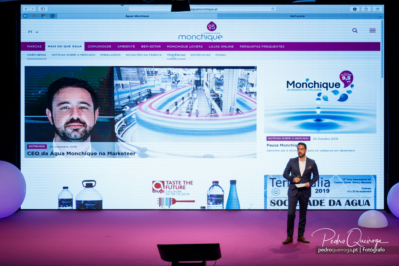 Orador em palco apresenta conteúdos da Água Monchique projetados em ecrã gigante durante evento corporativo