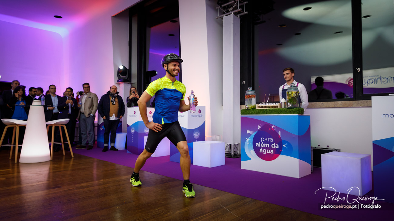 Ciclista apresenta garrafa em evento corporativo captado pelo fotógrafo Pedro Queiroga com iluminação roxa vibrante