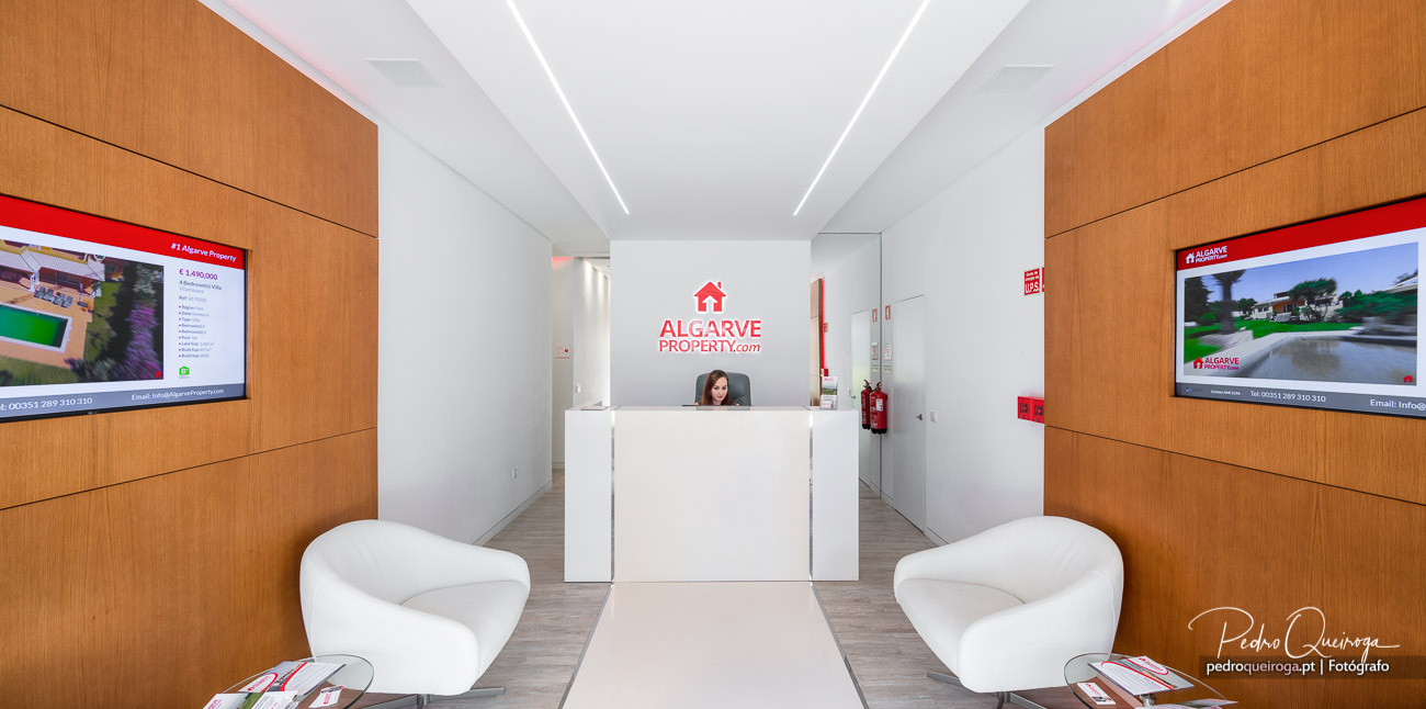 Receção moderna da Algarve Property com painéis em madeira, poltronas brancas e composições fotográficas nas paredes laterais