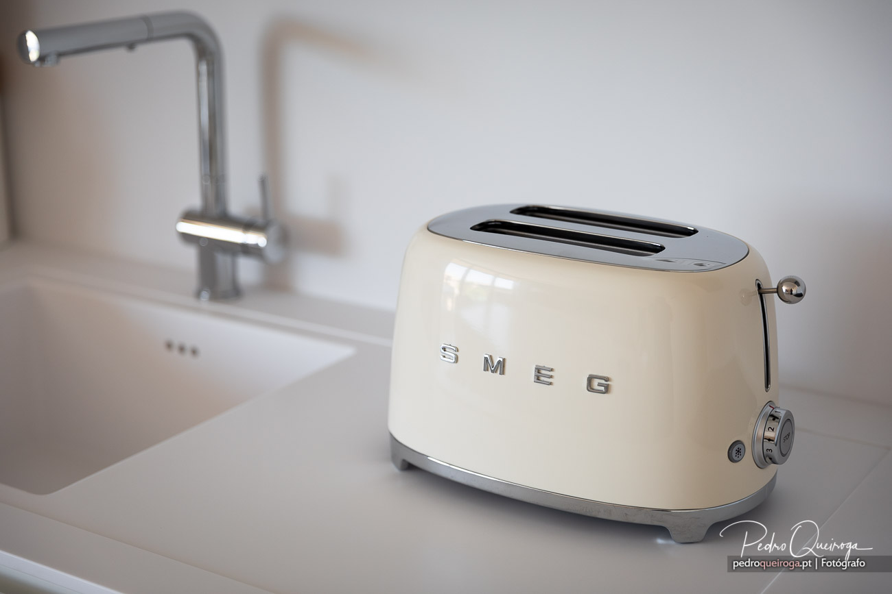Torradeira SMEG bege sobre bancada branca minimalista com torneira cromada desfocada ao fundo em cozinha moderna