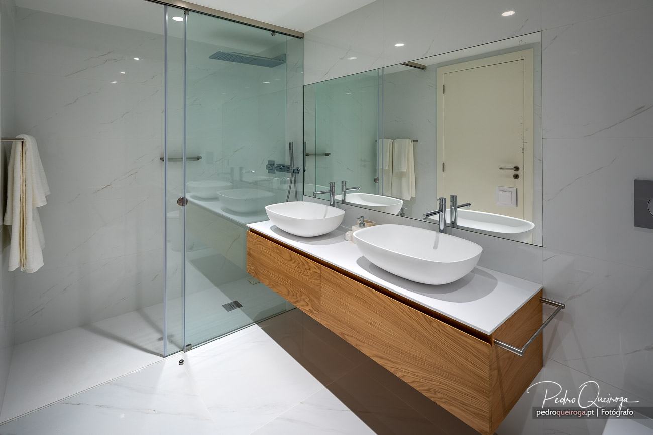 Casa de banho moderna com móvel suspenso em madeira, duas cubas ovais brancas e base de duche ampla em vidro