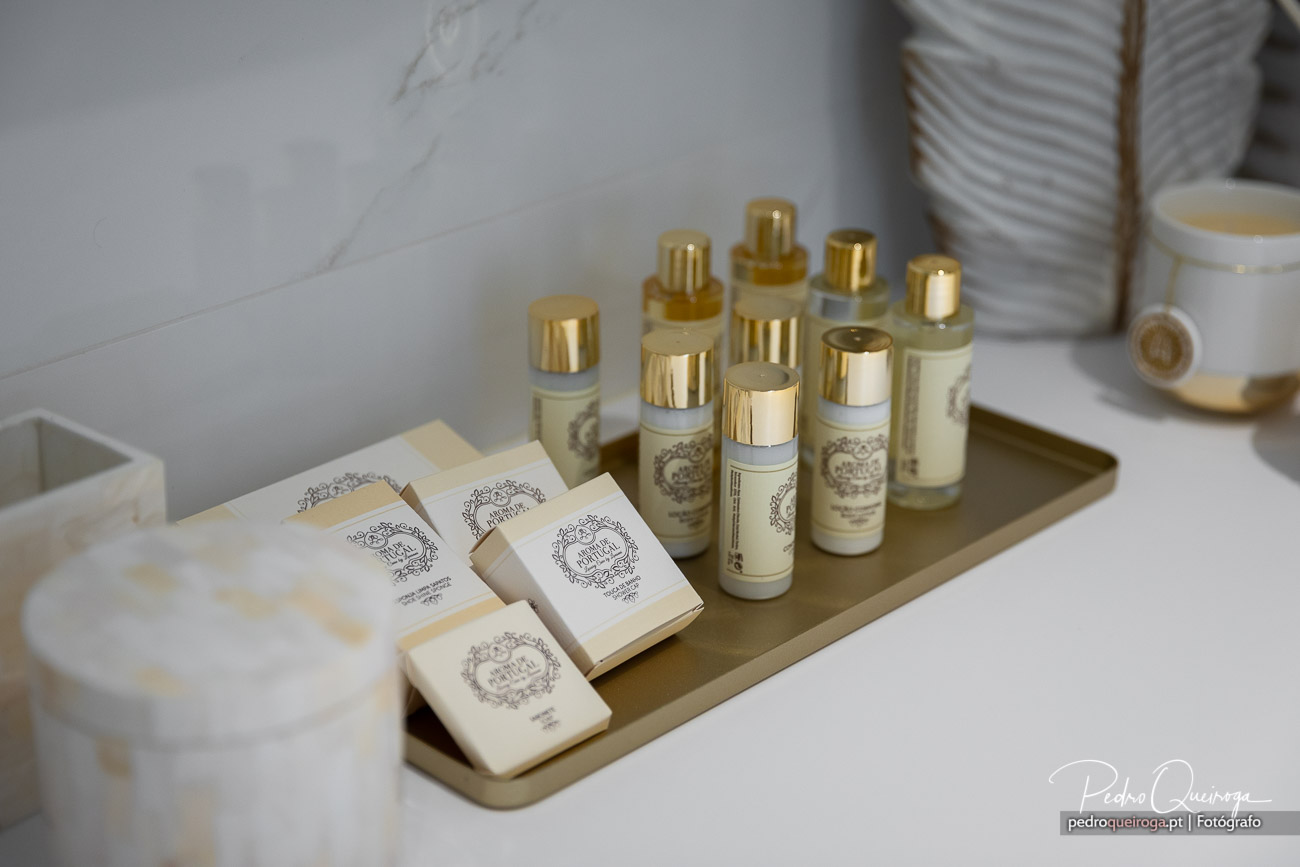 Conjunto elegante de amenities de banho com frascos dourados e sabonetes dispostos num tabuleiro bege sobre mármore branco