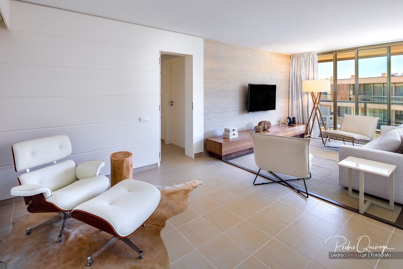 Sala de estar moderna com poltrona branca, móvel TV e ampla janela com luz natural abundante