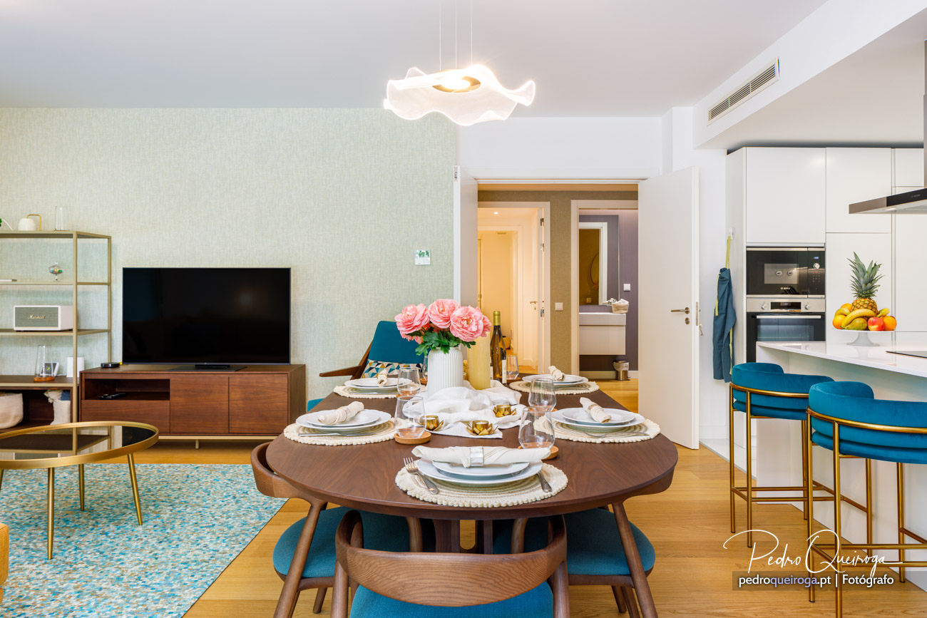 Sala de estar e jantar em conceito aberto, com decoração moderna, cadeiras azuis e mesa posta com flores cor-de-rosa