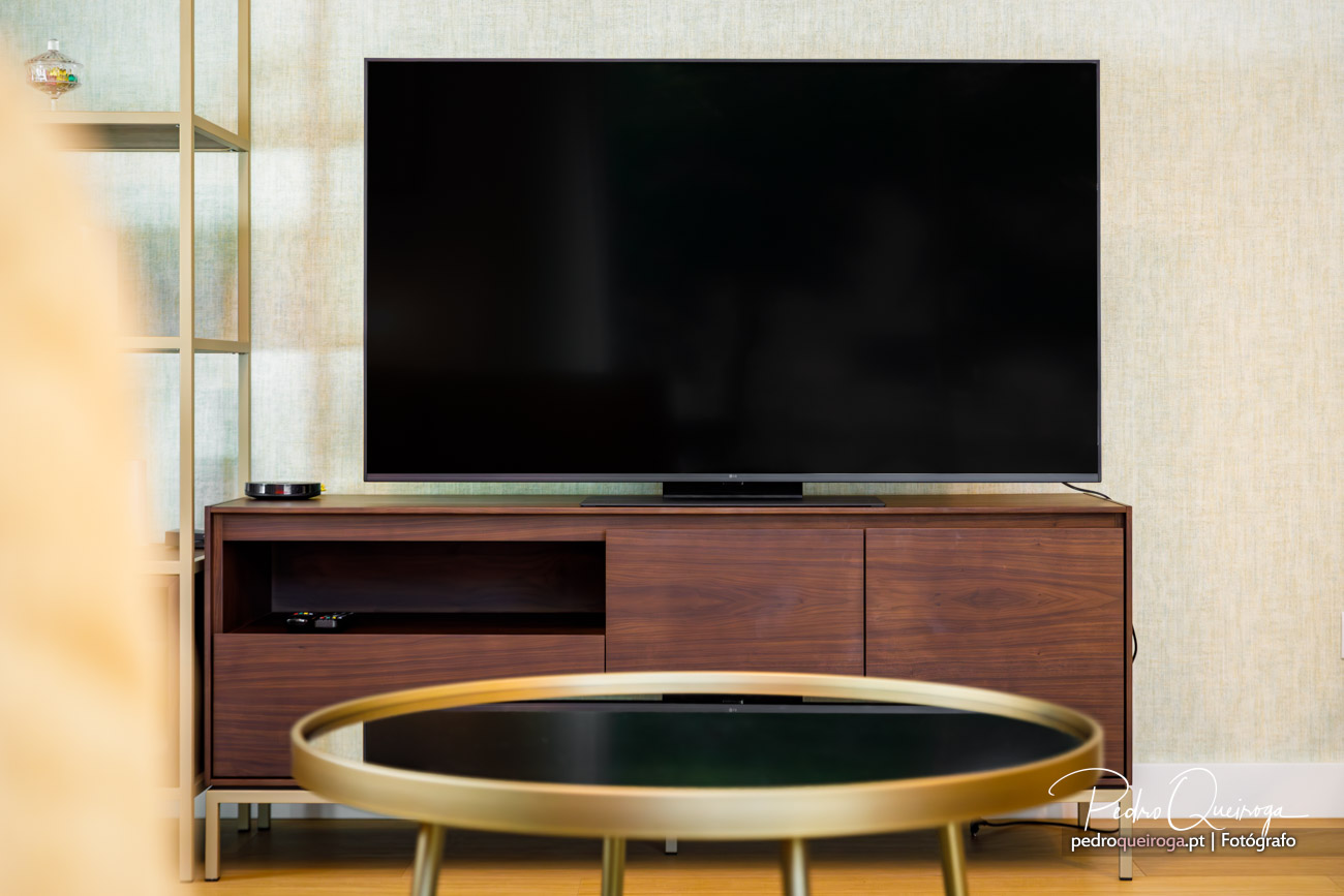 Sala de estar moderna com televisão de ecrã plano sobre móvel de madeira escura e mesa de centro dourada em primeiro plano