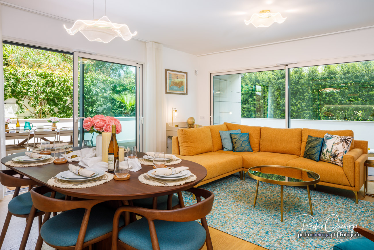 Sala de estar luminosa com sofá mostarda, mesa de jantar posta e decoração moderna com vista para o exterior