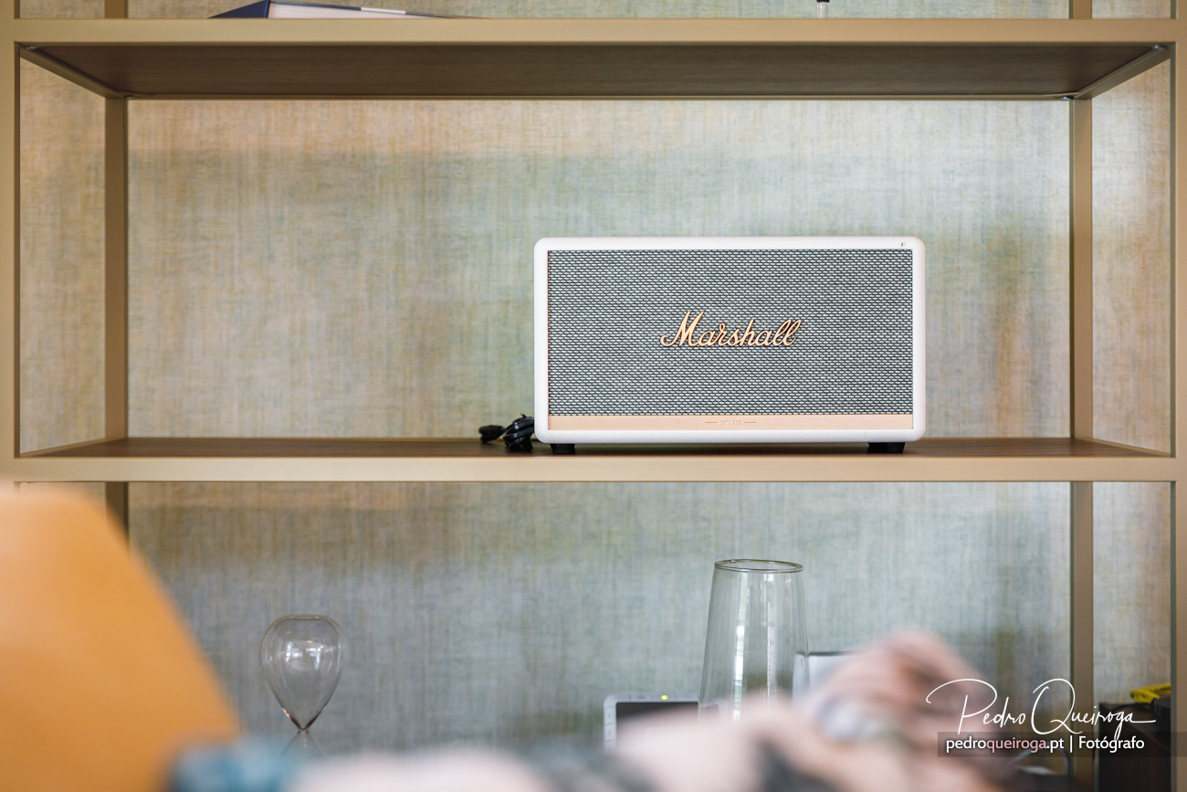 Coluna Marshall branca em prateleira de madeira com fundo azul suave e objetos decorativos em redor