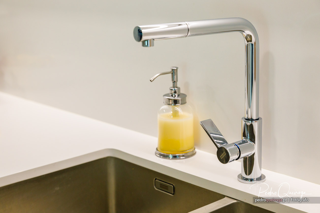 Torneira moderna cromada junto a lava-loiças com doseador de sabão amarelo sobre bancada branca minimalista