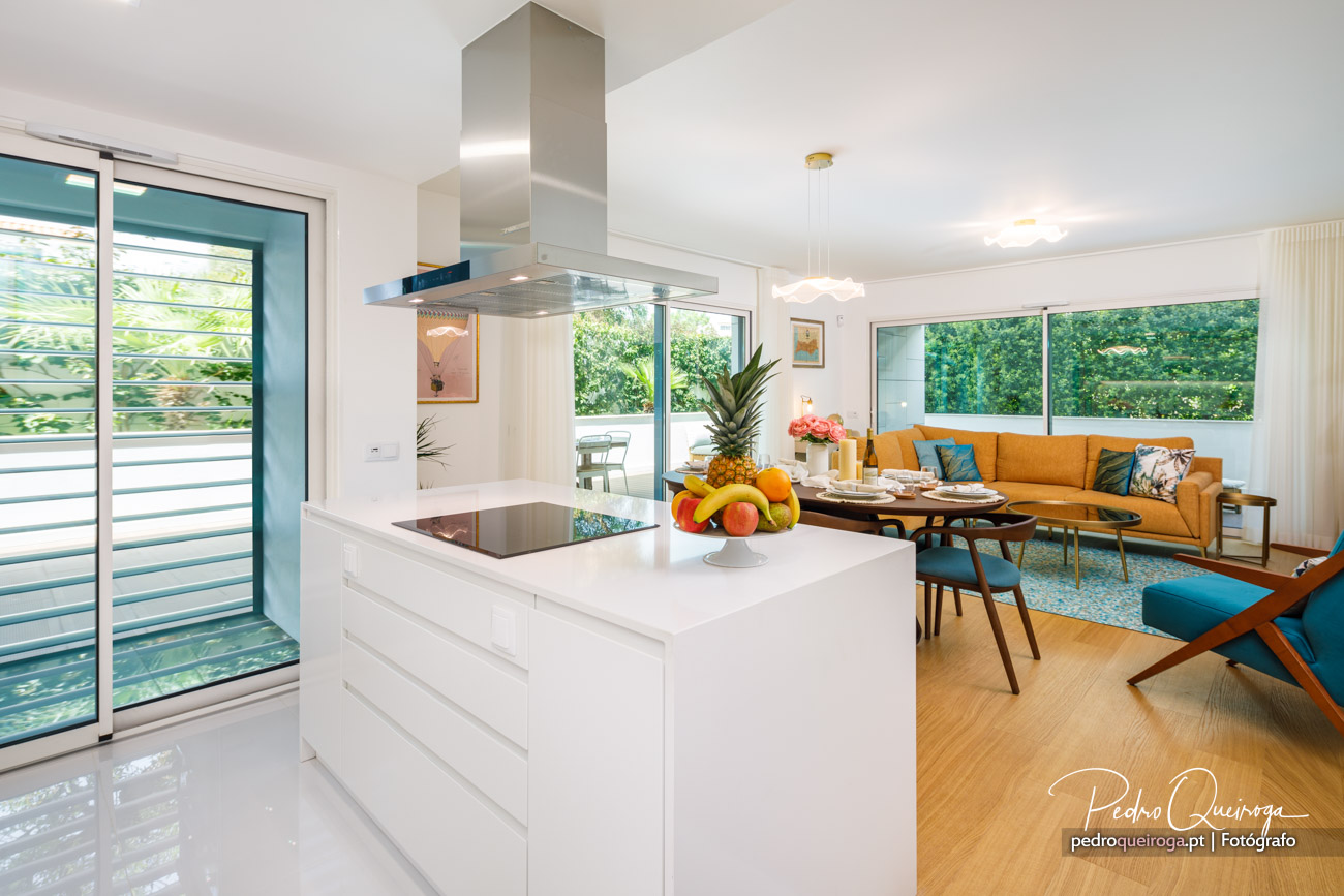 Sala moderna e luminosa com cozinha branca em ilha, sofá mostarda, janelas amplas e fruteira colorida ao centro