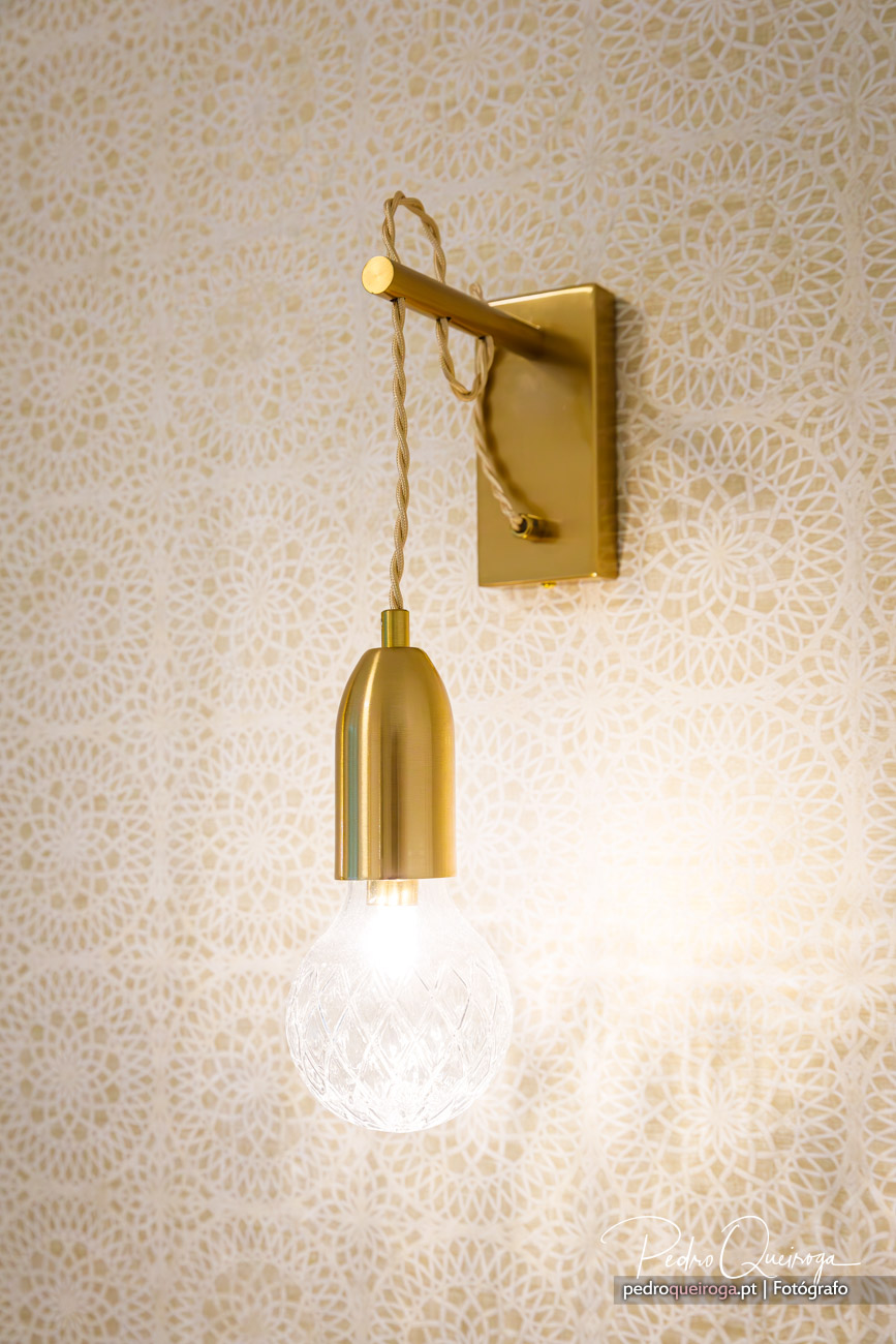 Candeeiro de parede dourado com cabo trançado e lâmpada decorativa contra papel de parede com padrão bege claro