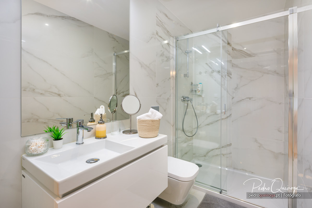 Casa de banho moderna com revestimento em mármore, lavatório suspenso branco e duche envidraçado amplo e luminoso.