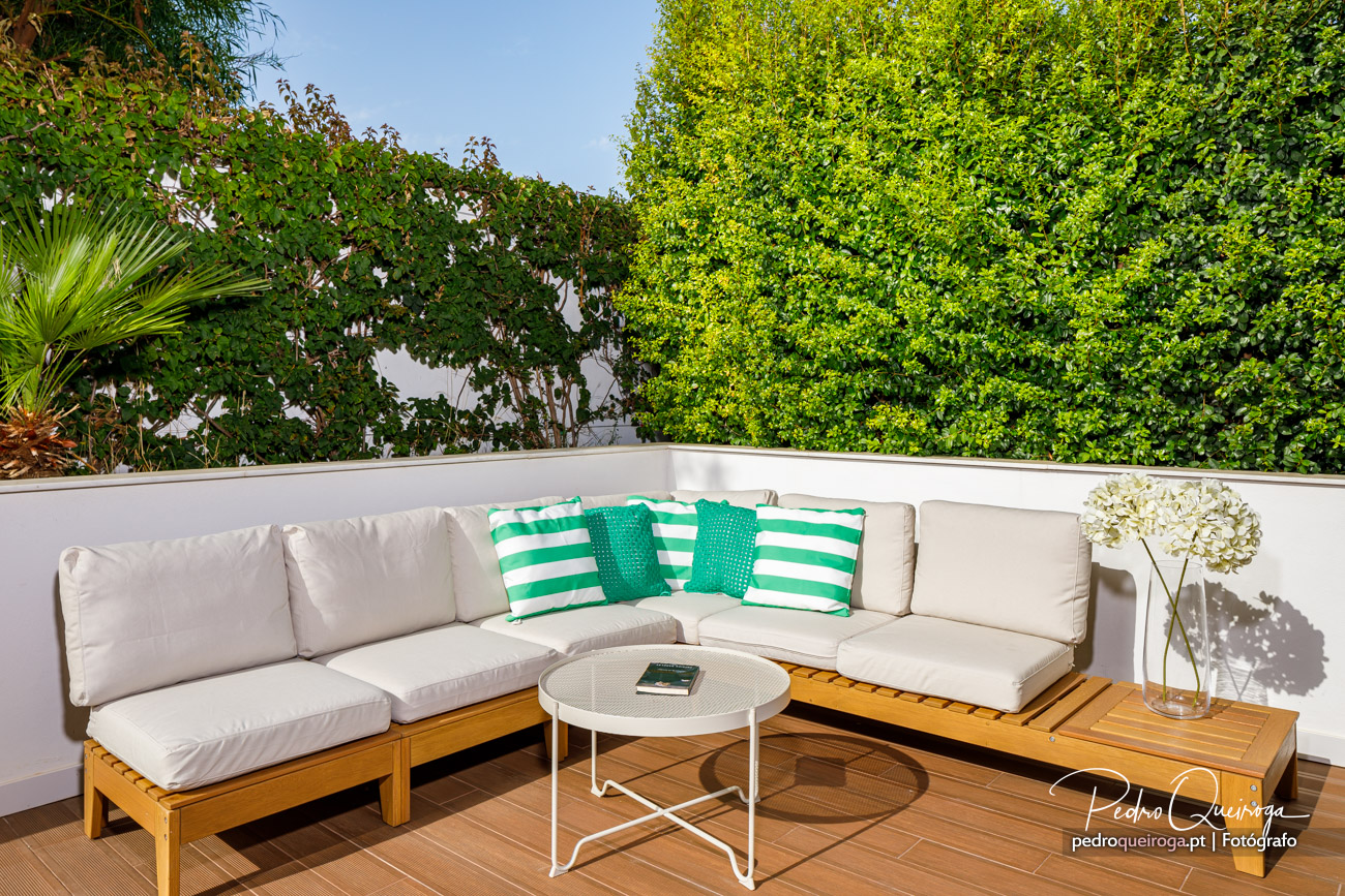 Terraço acolhedor com sofá em madeira, almofadas verdes e vegetação exuberante, harmonizando arquitetura e natureza.