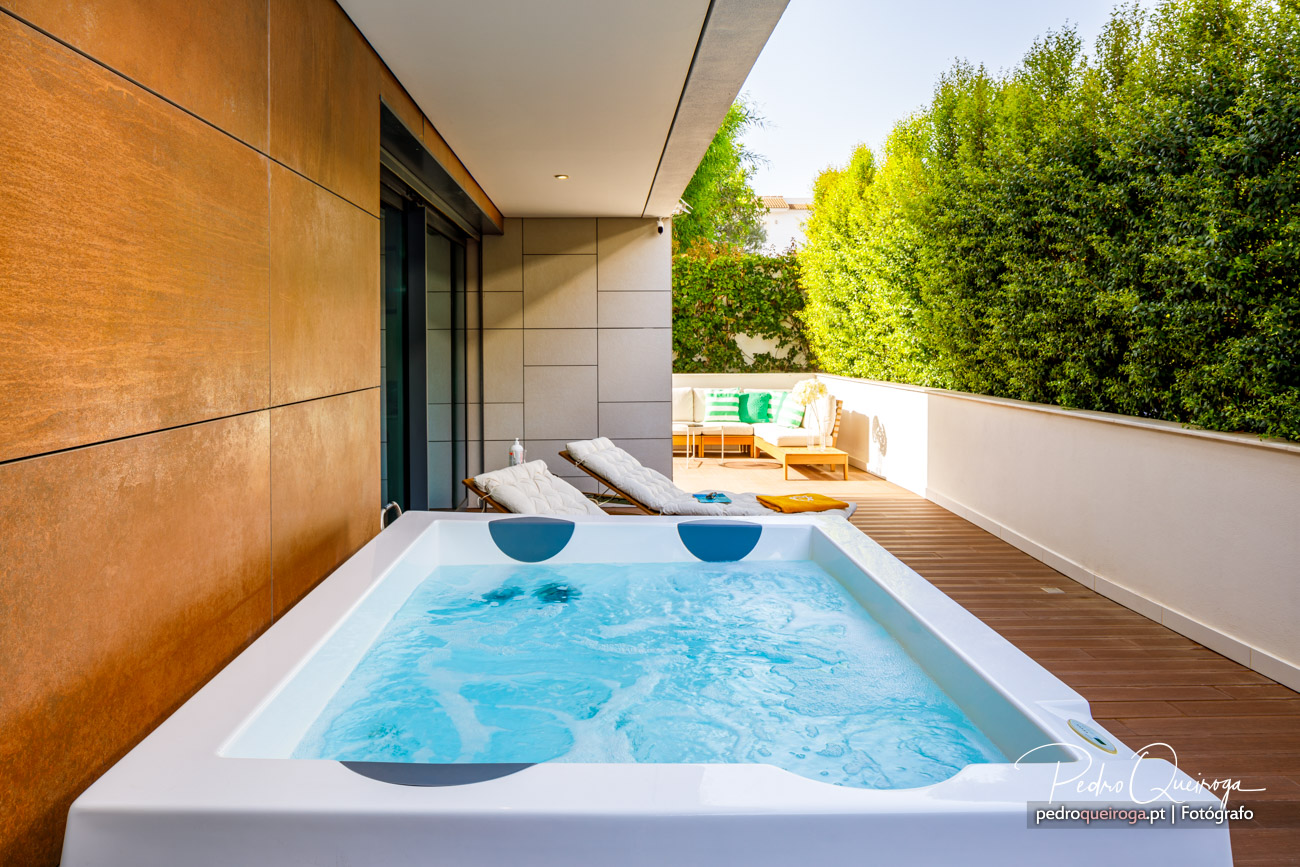 Jacuzzi exterior em terraço moderno com deck de madeira, espreguiçadeiras e vegetação abundante ao fundo