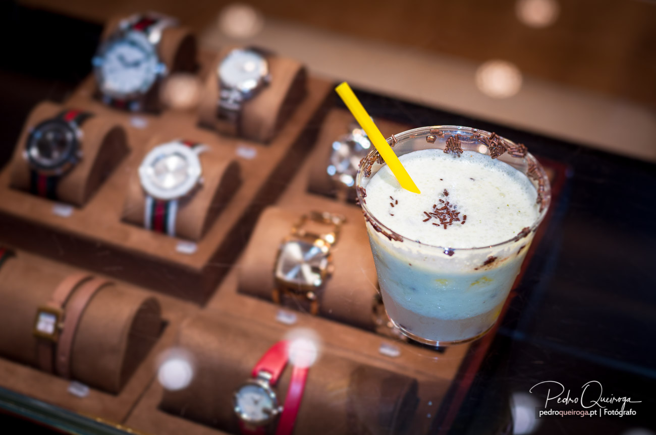 Bebida cremosa com raspas de chocolate e palhinha amarela junto a expositor de relógios em madeira