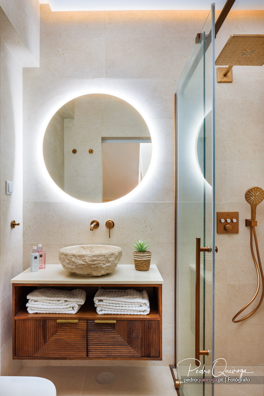 Casa de banho moderna com espelho circular retroiluminado, lavatório em pedra e acabamentos dourados elegantes