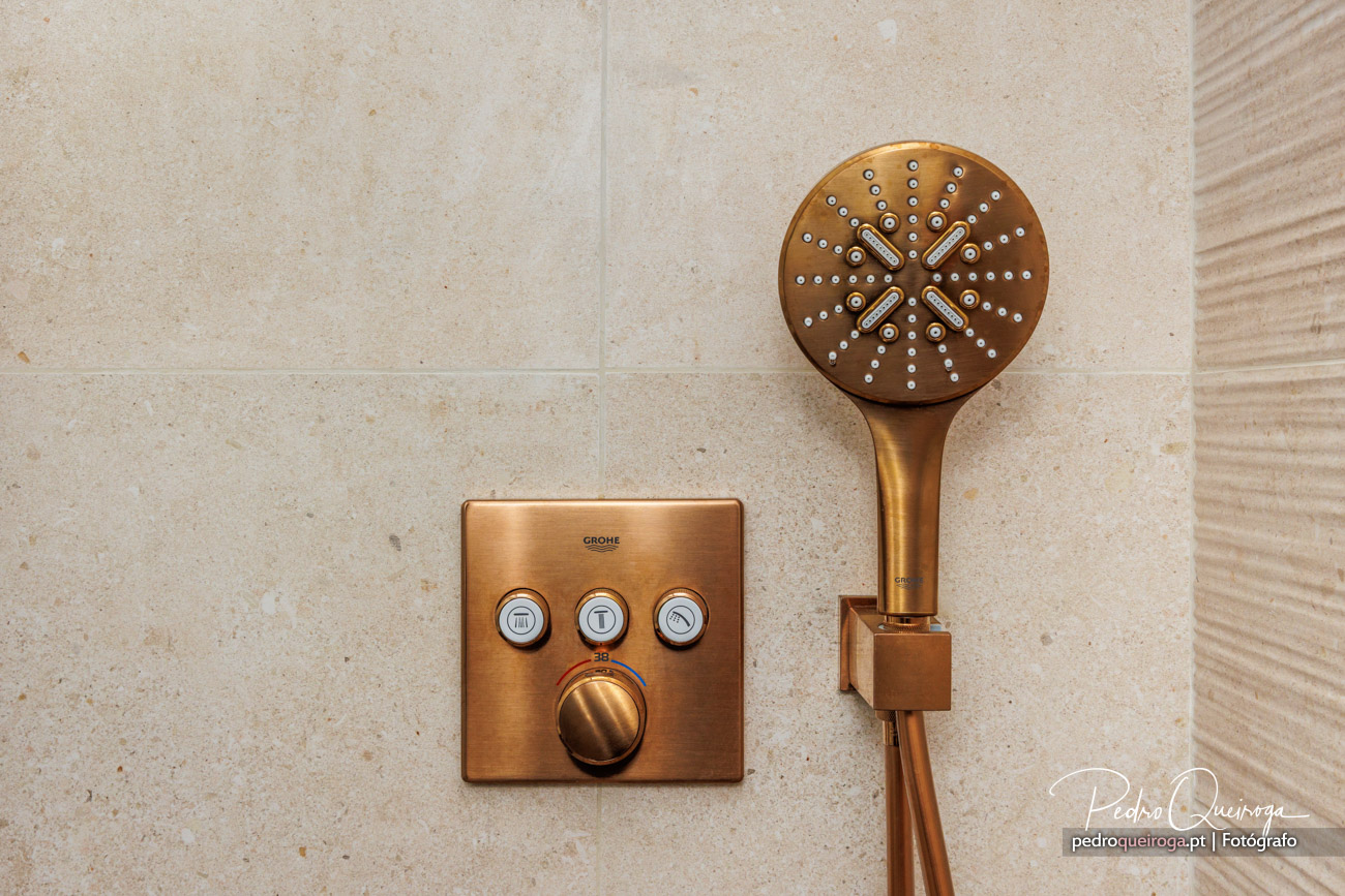 Chuveiro de mão e comando termostático em bronze fixos numa parede de casa de banho em tons bege