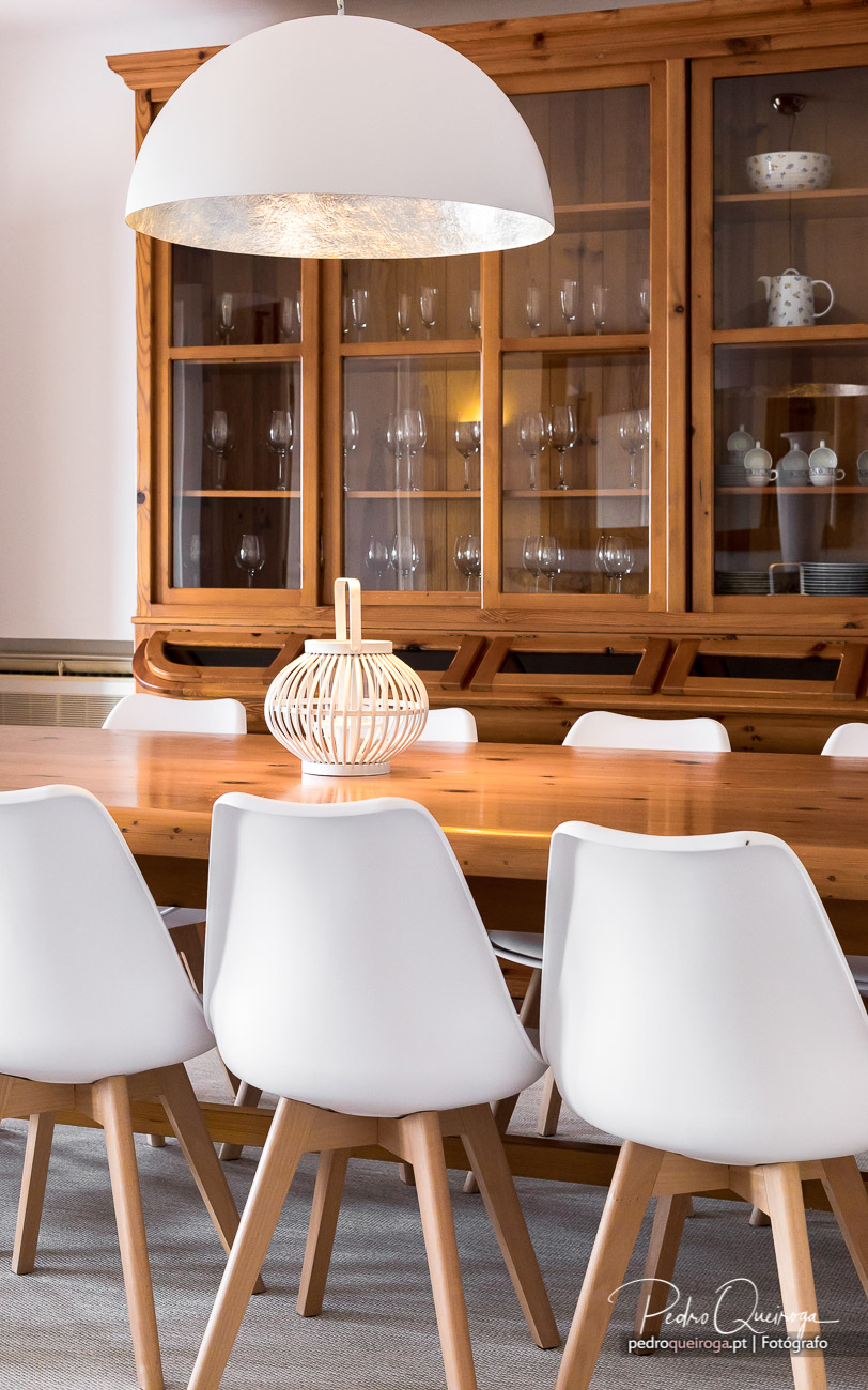 Sala de jantar com mesa em madeira, cadeiras brancas e cristaleira, captada em fotografia de interiores