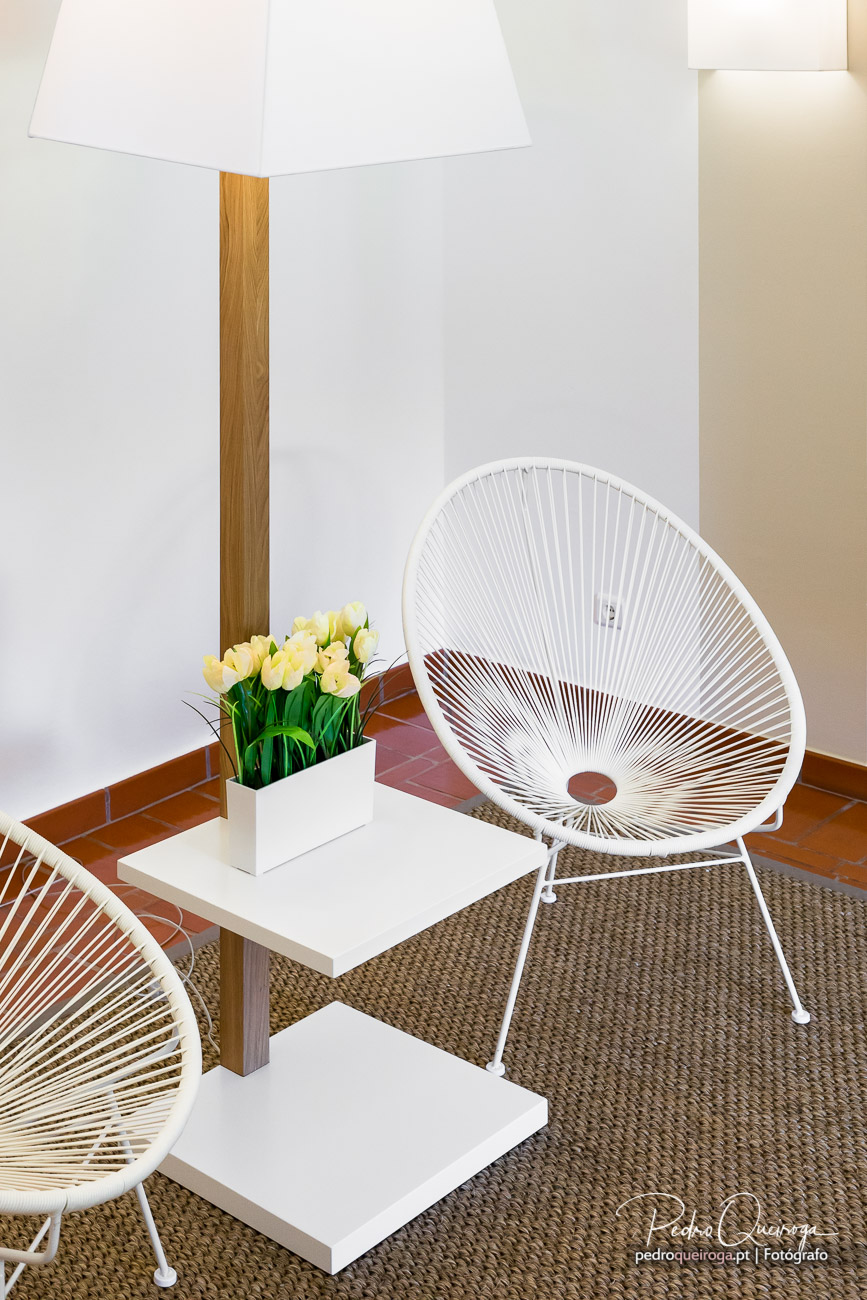 Cadeira branca em estrutura de corda sobre tapete de sisal, mesa lateral com tulipas amarelas e candeeiro de pé em madeira