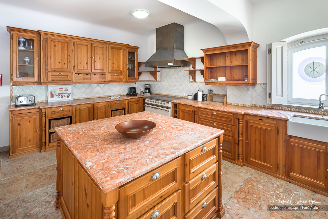 Cozinha ampla com móveis em madeira natural, ilha central com tampo em mármore rosa e exaustor metálico