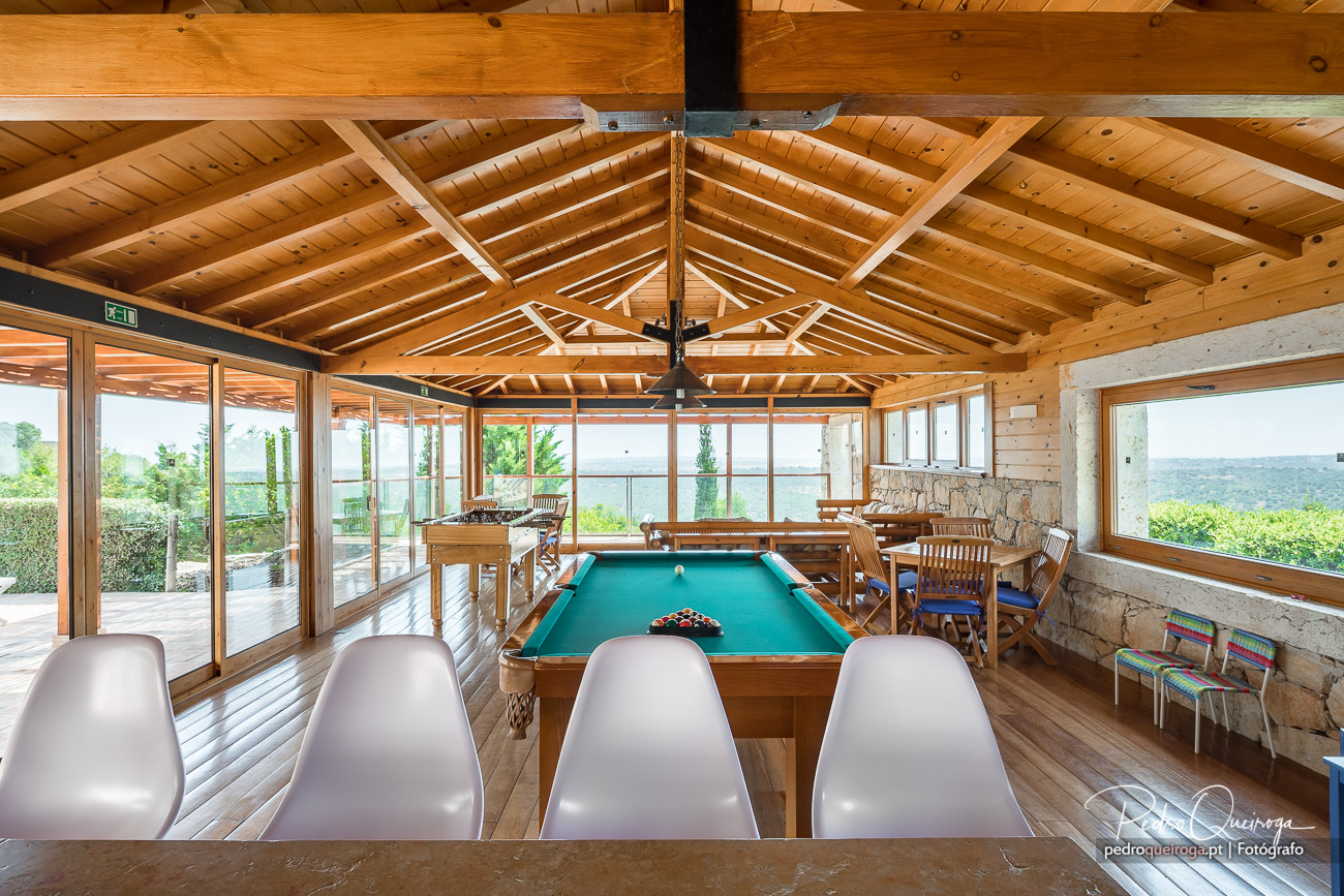 Sala de jogos ampla com teto em madeira, mesa de bilhar, janelas panorâmicas e vista para o exterior