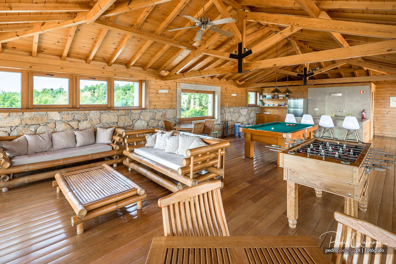 Sala de estar ampla em madeira com teto alto, mobiliário rústico, mesa de matraquilhos, bilhar e zona de refeições