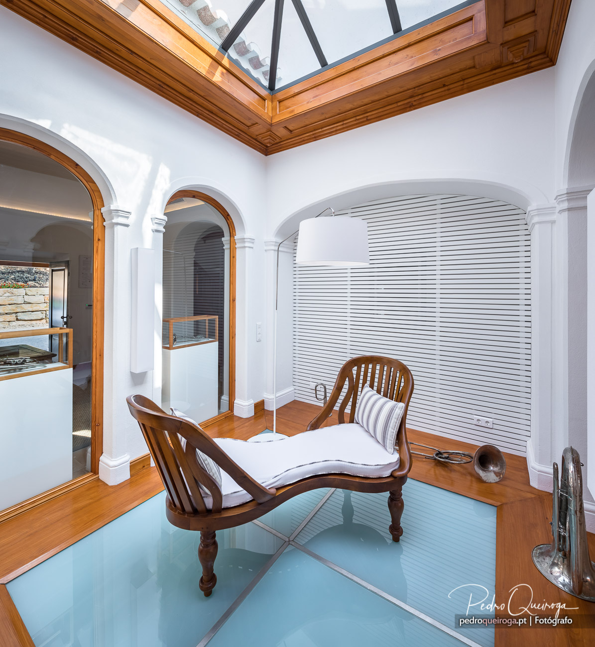 Claraboia em madeira ilumina sala com arcos, espreguiçadeira e claraboia num imóvel elegante e luminoso.