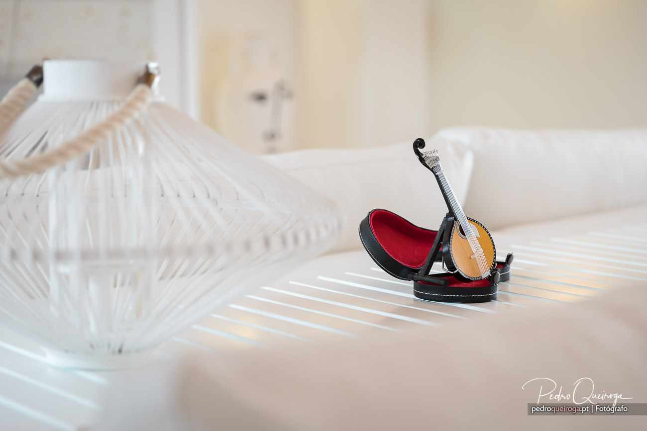 Miniatura de guitarra portuguesa em estojo com forro vermelho sobre mesa branca junto a lanterna decorativa