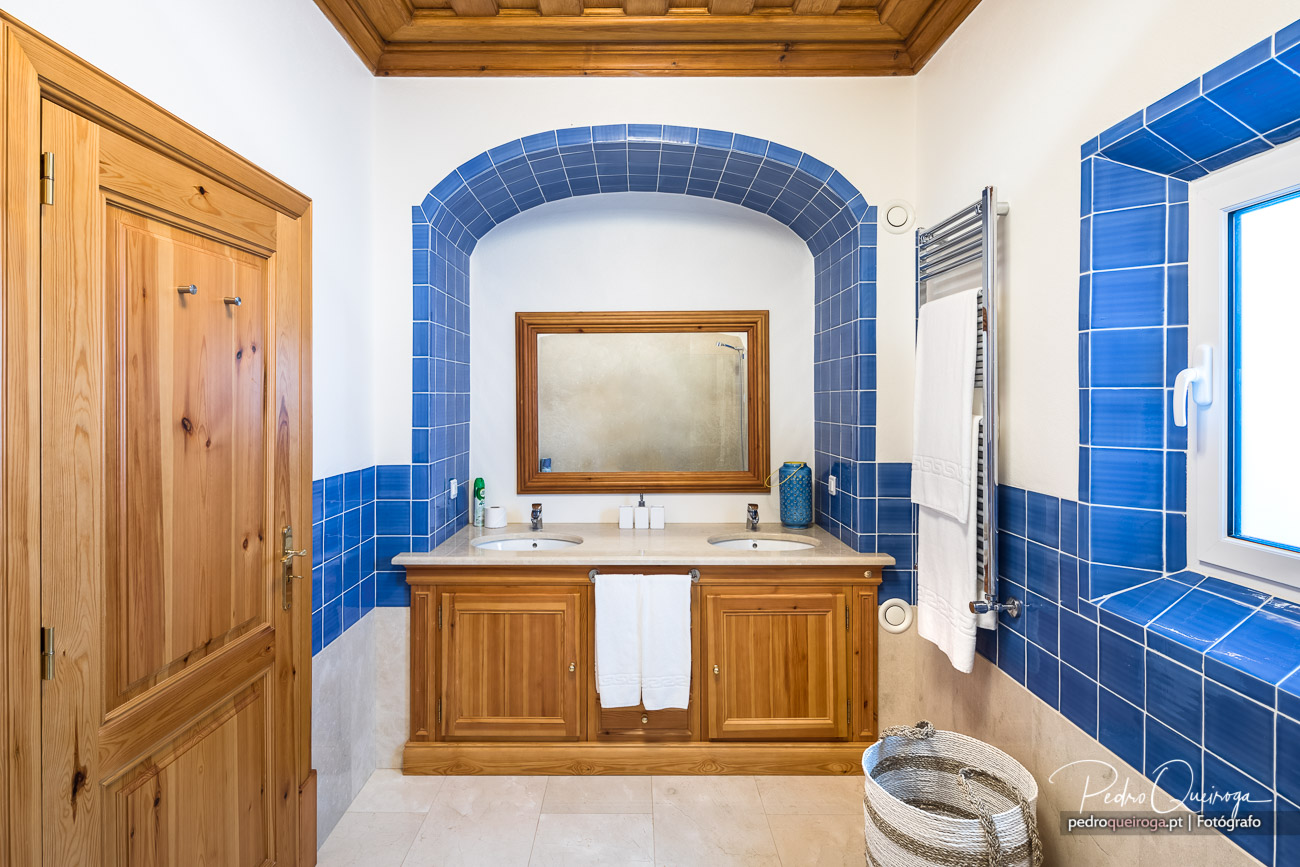 Casa de banho com arquitetura elegante, arco revestido a azulejo azul, móvel duplo em madeira e teto trabalhado