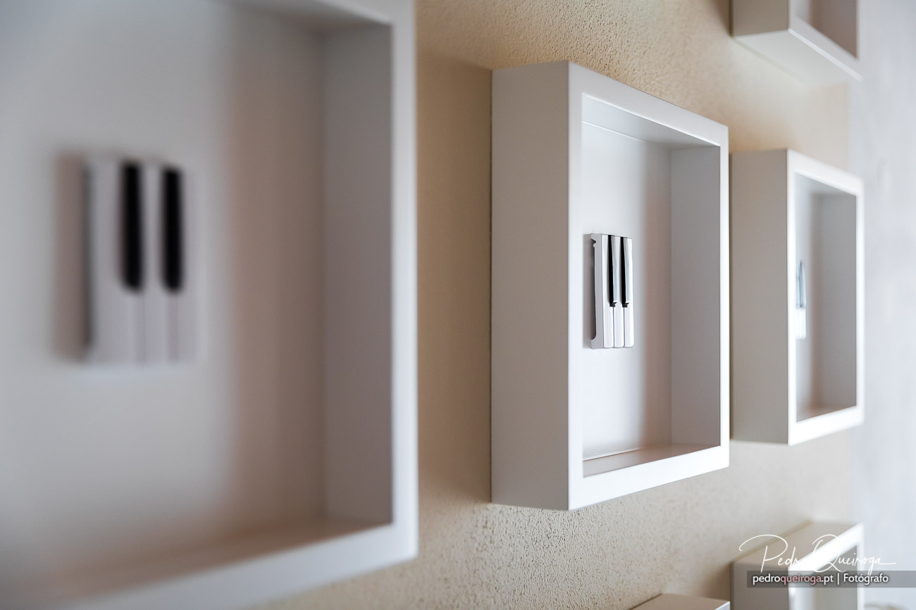 Quadros brancos com teclas de piano em moldura, alinhados na parede bege de um corredor minimalista