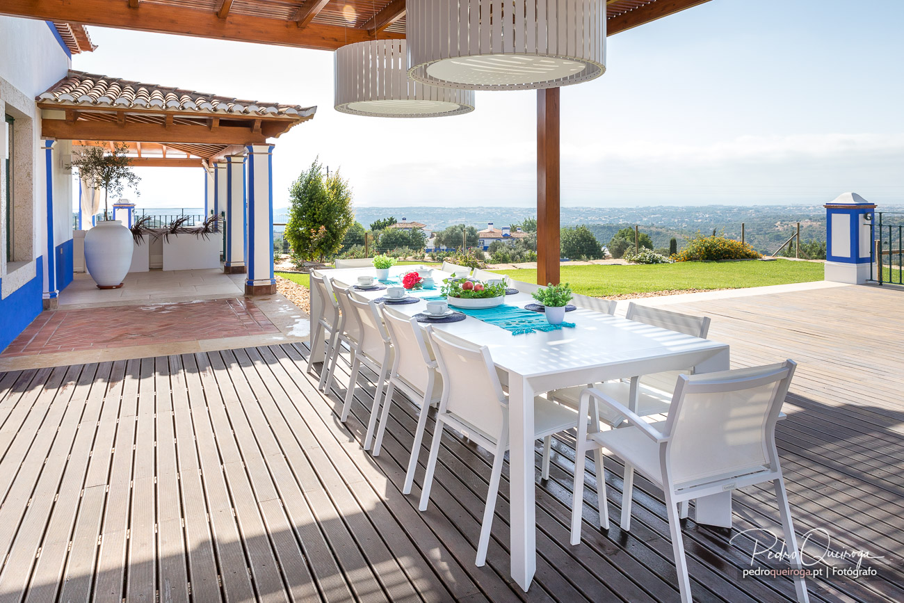 Terraço amplo em deck de madeira com mesa branca, jardim verdejante e vista panorâmica sobre a paisagem