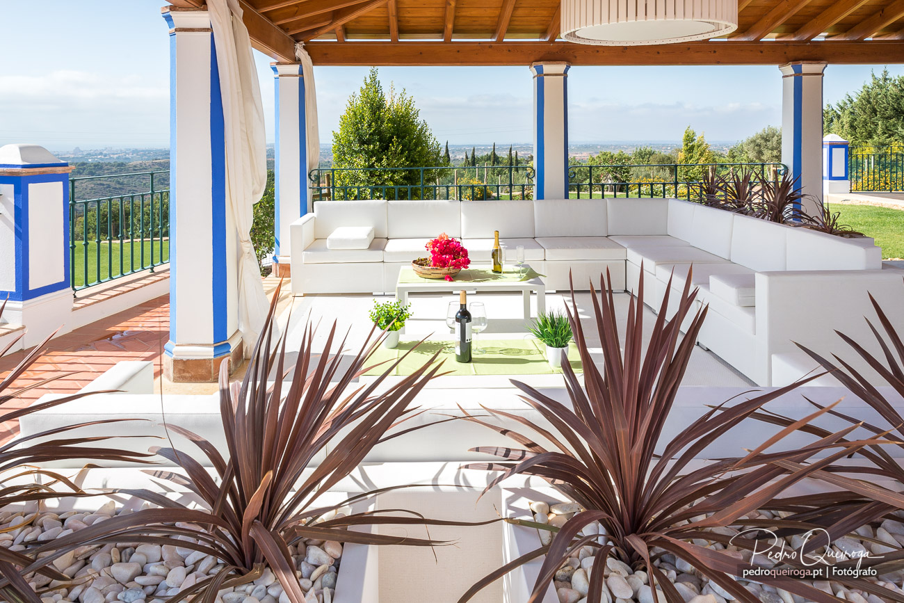 Terraço coberto com mobiliário branco, plantas decorativas e vista panorâmica sobre jardins e paisagem ao fundo