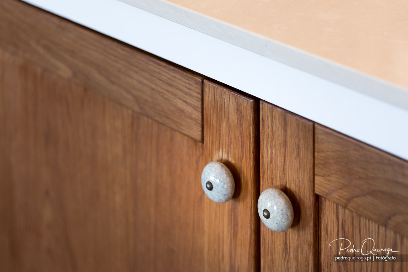 Móvel de cozinha em madeira com tampo branco e puxadores redondos em pedra clara com detalhe em metal escuro