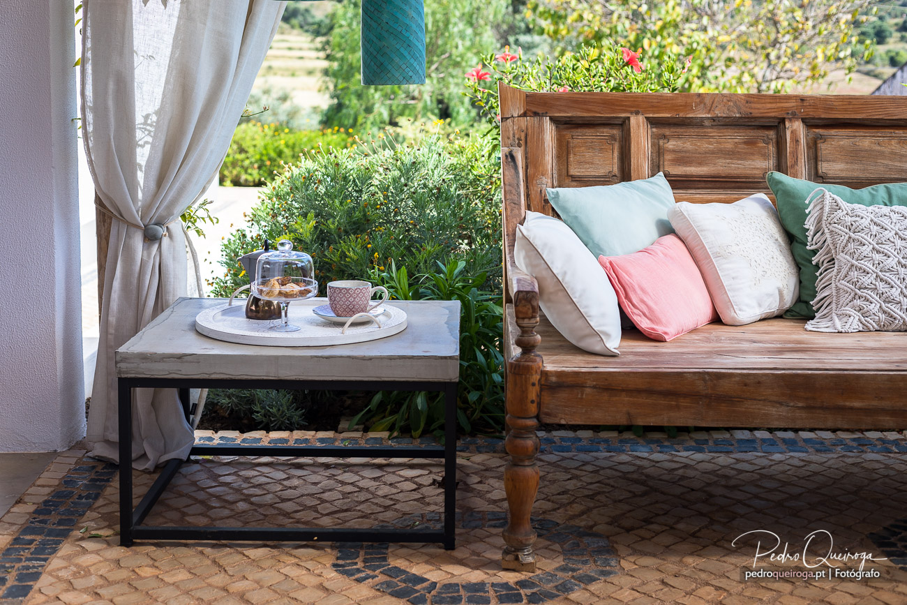 Composição fotográfica de terraço acolhedor com banco rústico, almofadas coloridas e mesa de café ao ar livre