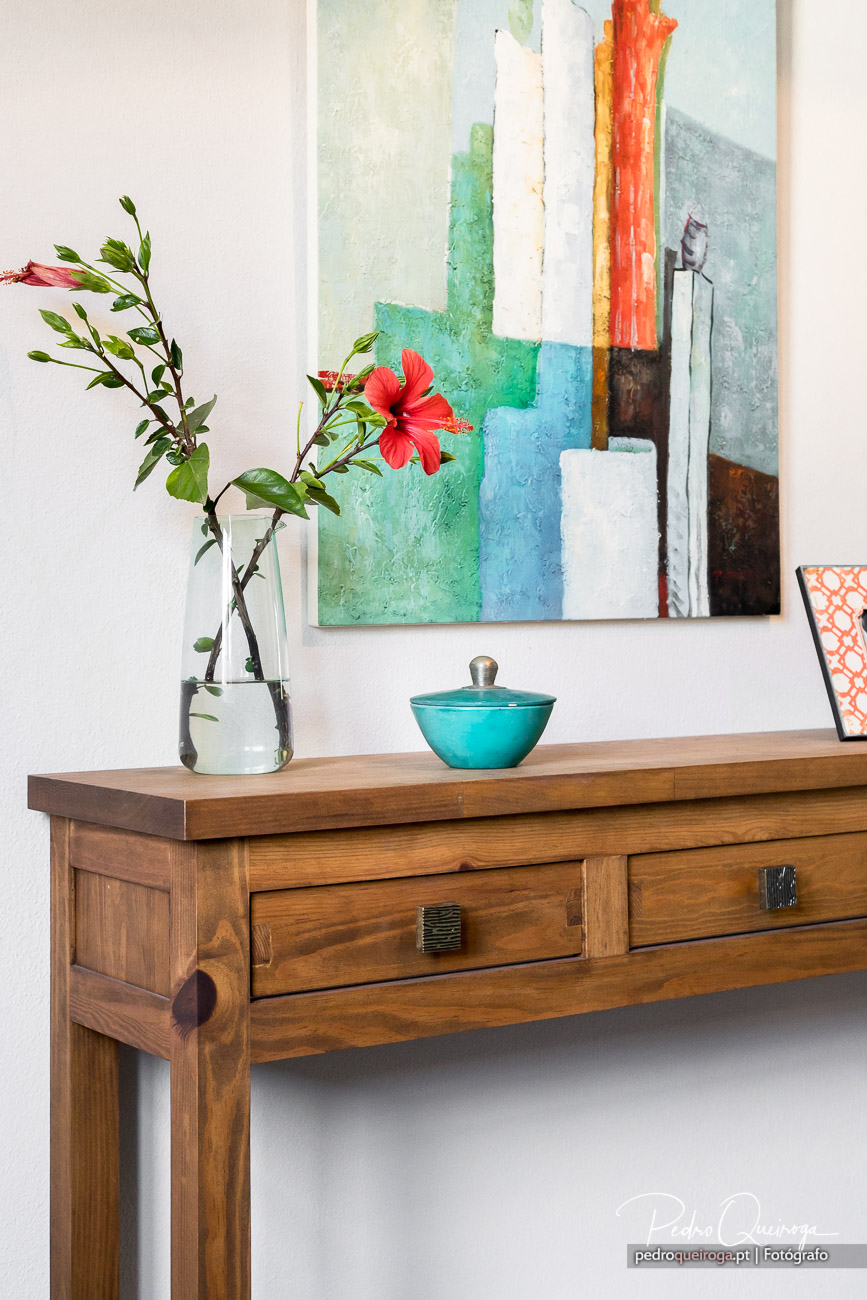 Aparador de madeira com hibisco vermelho em jarro e quadro abstrato colorido, ideal para hotéis e interiores modernos