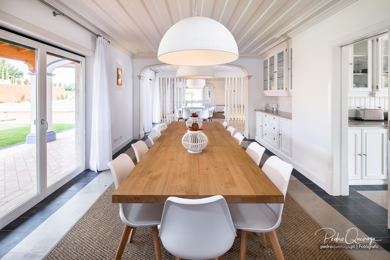 Sala de jantar luminosa com mesa em madeira maciça, cadeiras brancas e teto em madeira branca lacada