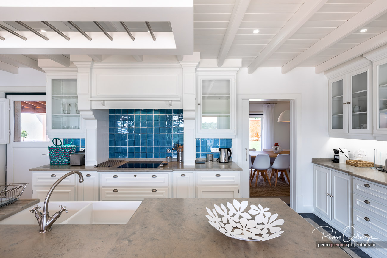 Cozinha ampla e luminosa com armários brancos, azulejos azuis vibrantes e bancadas em pedra clara com detalhes decorativos