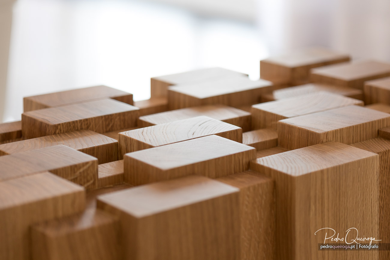 Blocos de madeira com diferentes alturas e tons, criando uma composição geométrica e orgânica sobre fundo claro.