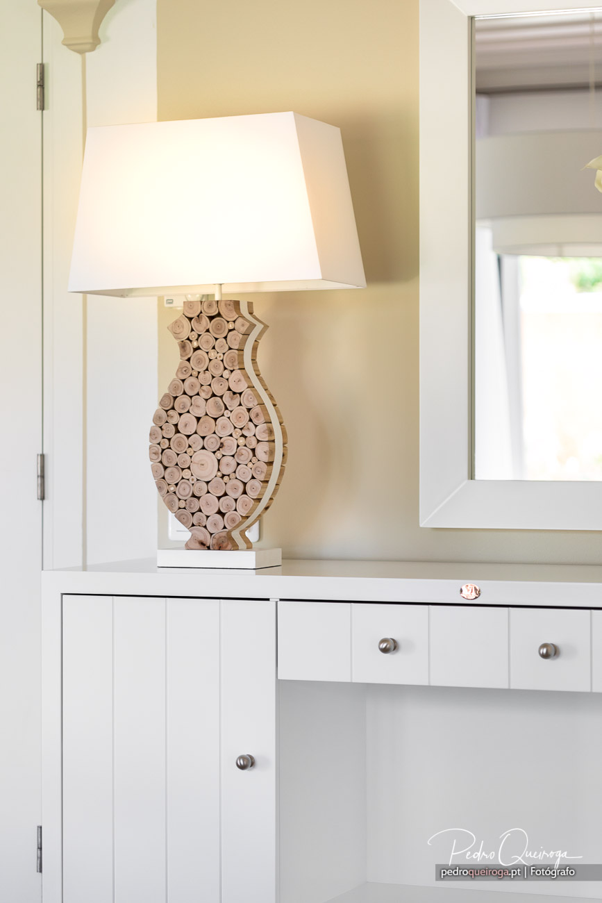 Candeeiro decorativo com base em madeira natural sobre cómoda branca em quarto luminoso e acolhedor