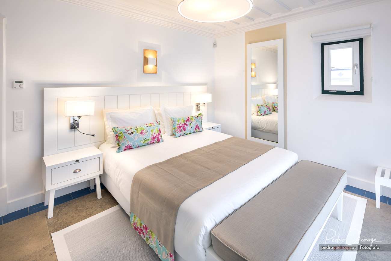 Quarto luminoso com decoração clara e almofadas floridas, captado em composição fotográfica profissional de interiores.