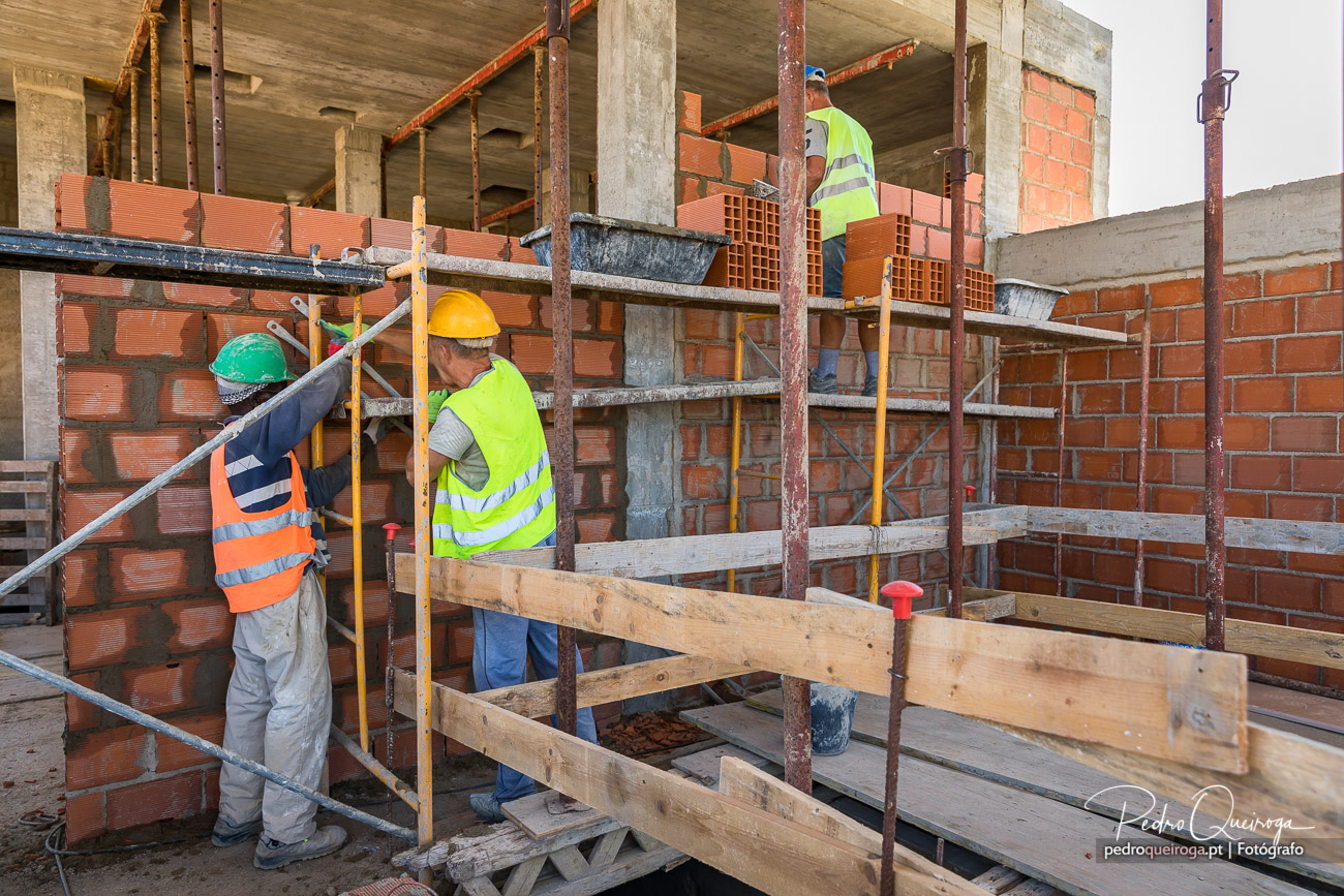 Operários de construção civil a assentar tijolos em andaime metálico no interior de estrutura em betão armado