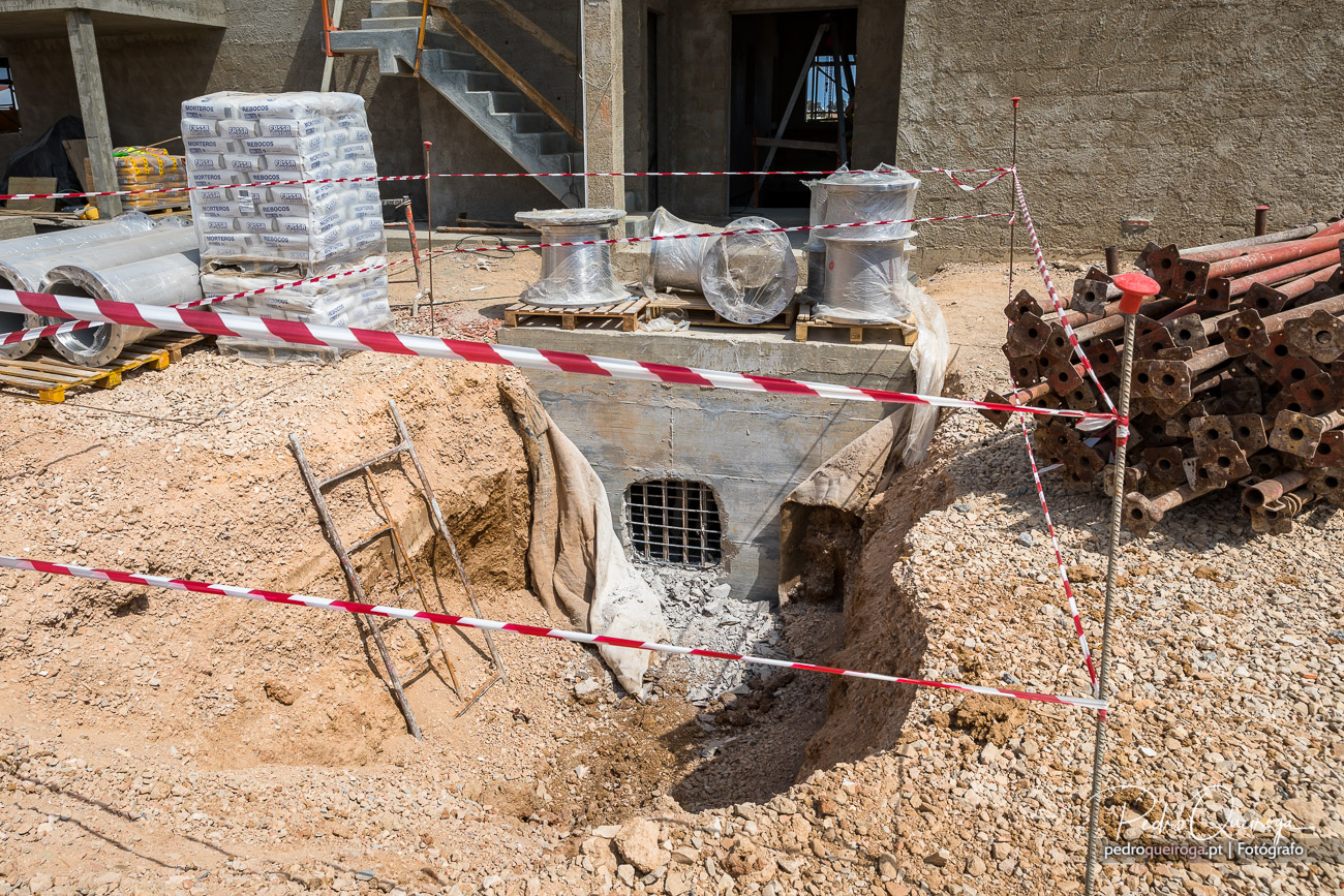 Caixa de betão em escavação com grelha metálica e fita de sinalização vermelha e branca em estaleiro de construção civil
