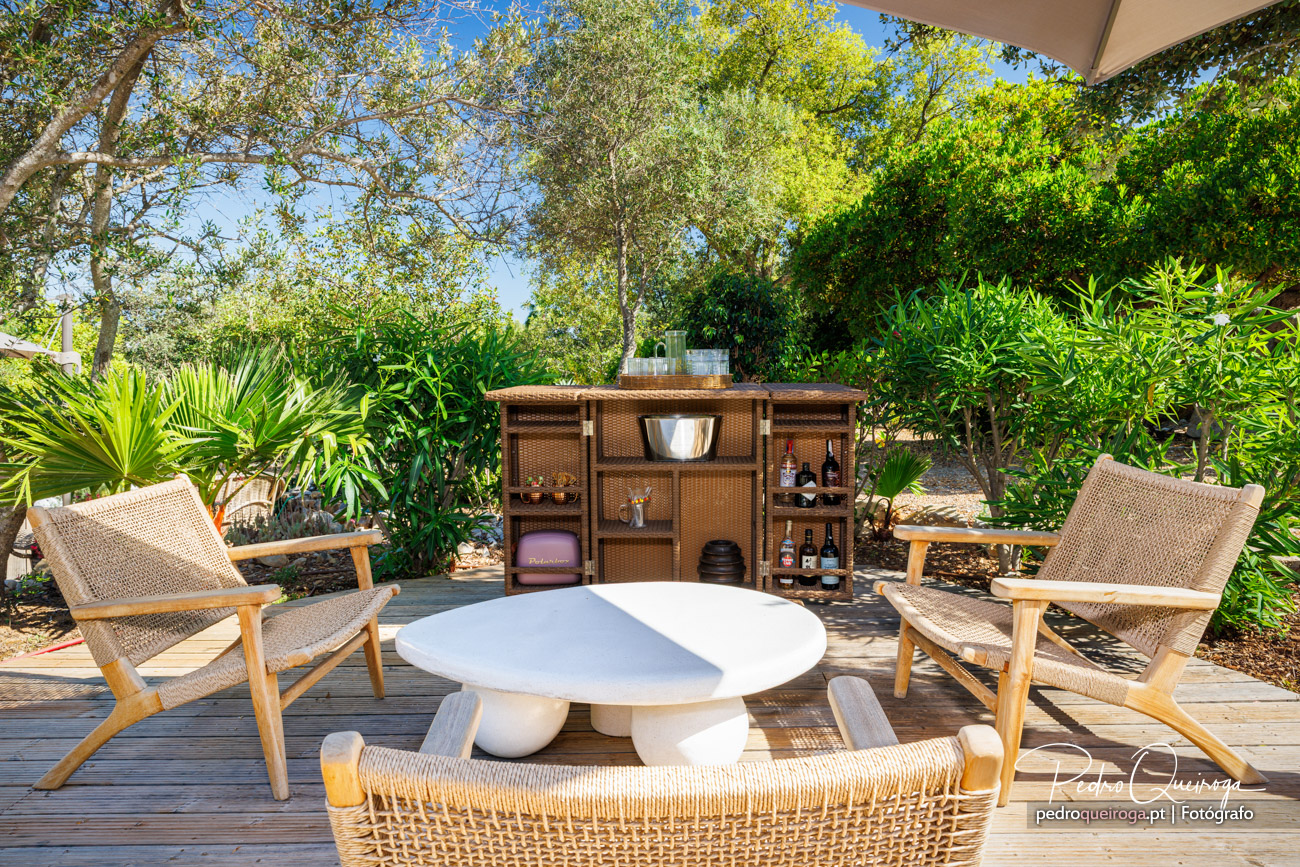 Terraço acolhedor com mesa branca, cadeiras em rattan, bar de vime e vegetação exuberante sob céu azul
