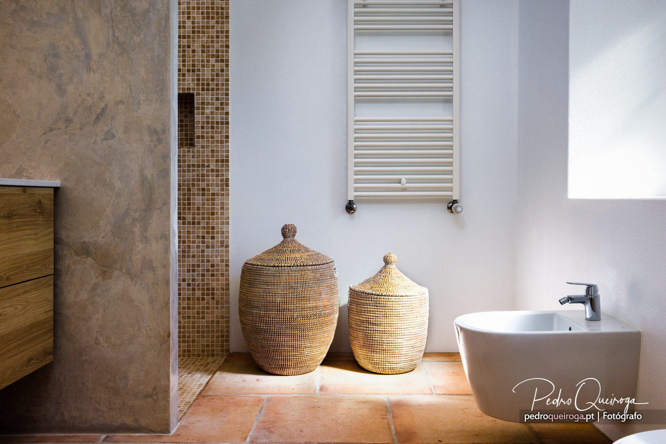 Casa de banho moderna com cestos artesanais, mosaico dourado, toalheiro metálico e lavatório branco minimalista