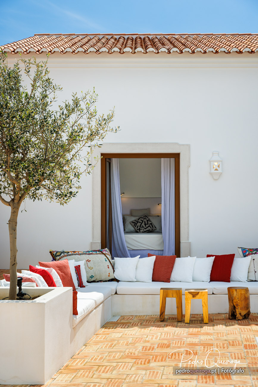 Pátio mediterrânico com oliveira, sofás brancos e almofadas coloridas captado por fotógrafo de arquitetura