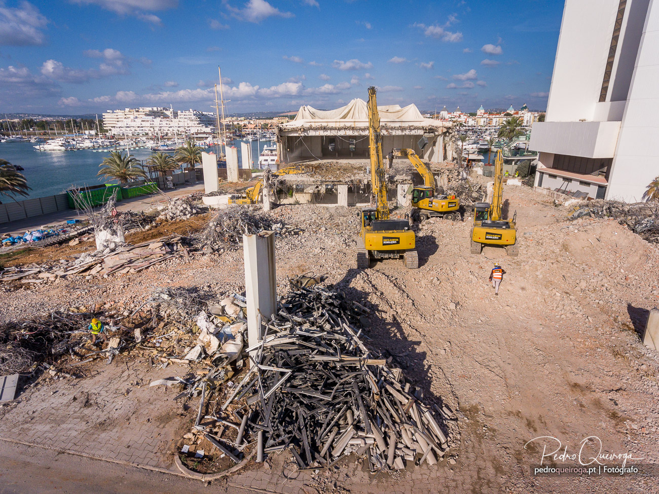Escavadoras a demolir estrutura de betão com cobertura em lona junto à marina de Vilamoura, Algarve
