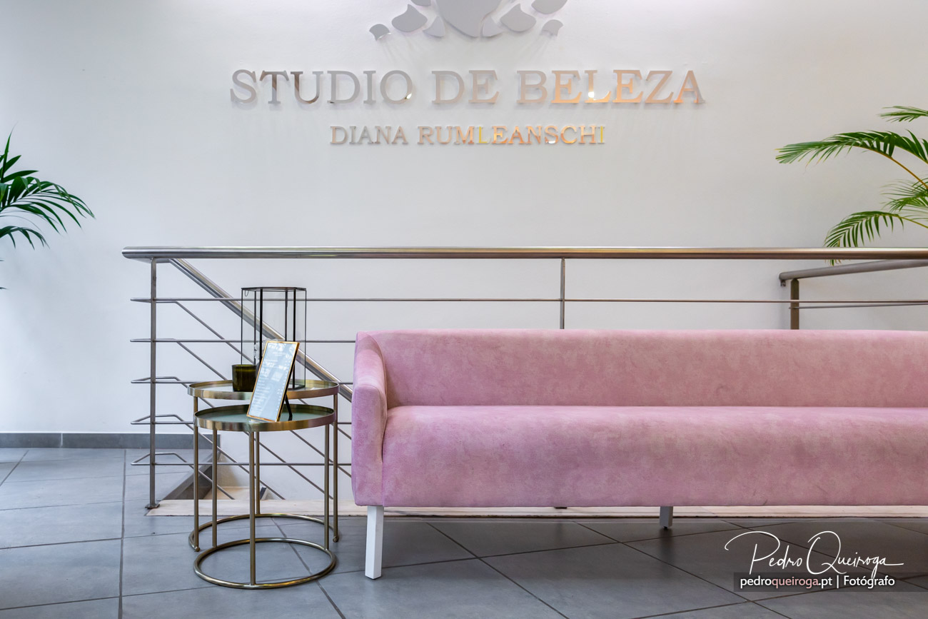 Sala de espera com sofá rosa, mesas douradas e letreiro Studio de Beleza Diana Rumleanschi na parede branca.