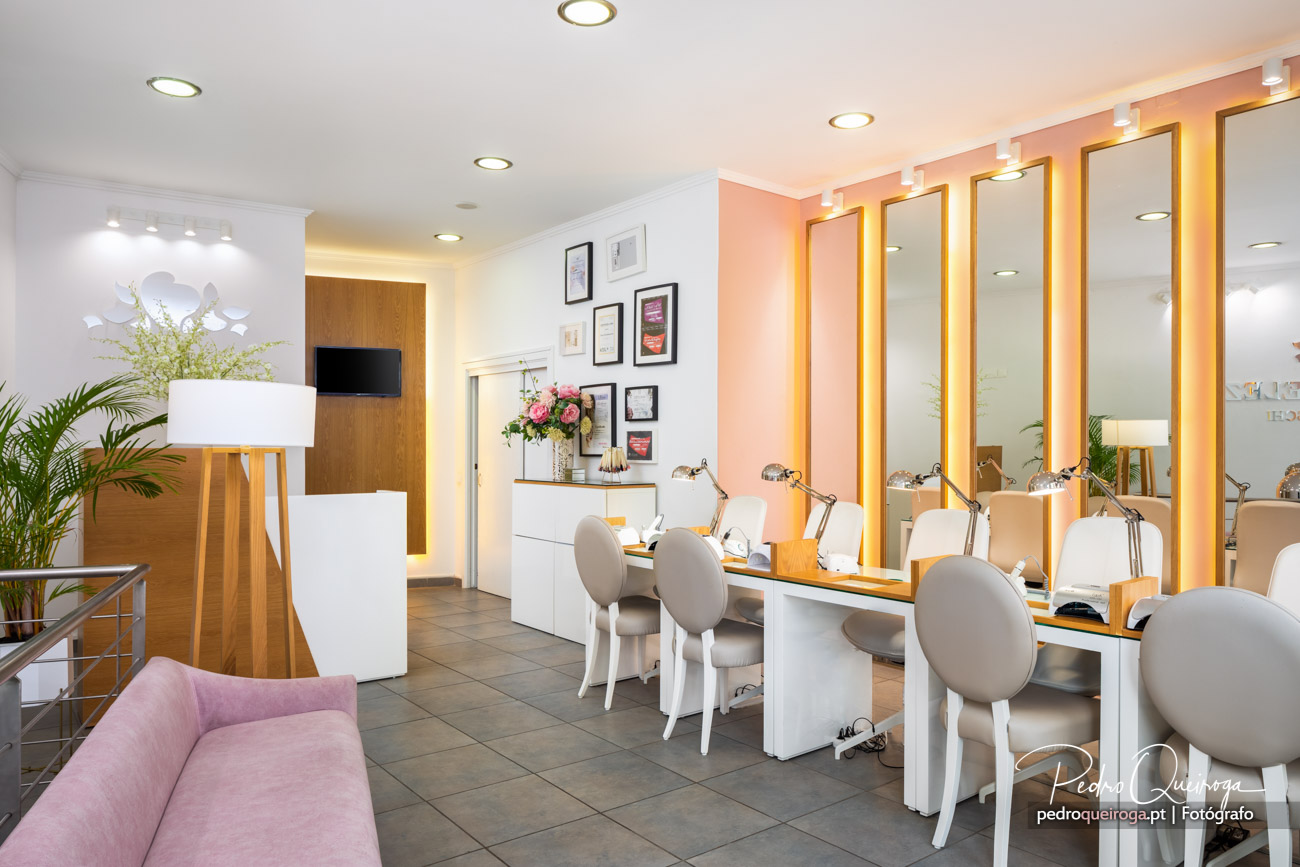 Salão de beleza moderno com espelhos iluminados, cadeiras brancas, decoração em tons rosa e branco, plantas naturais.